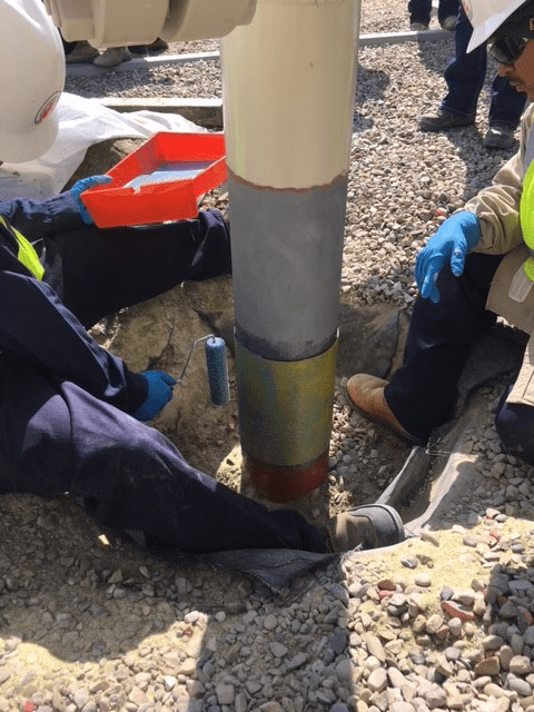 Installers secure Snap Wrap to strengthen a pipe and protect it at the air/soil interface.